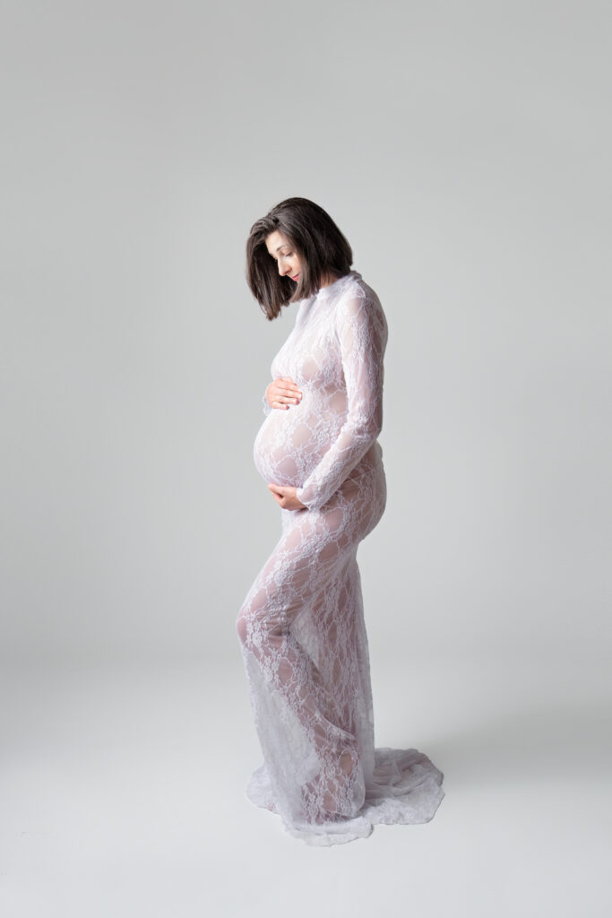Zwangere vrouw in witte kanten jurk tijdens een zwangerschap fotoshoot bij Little Miracle memories