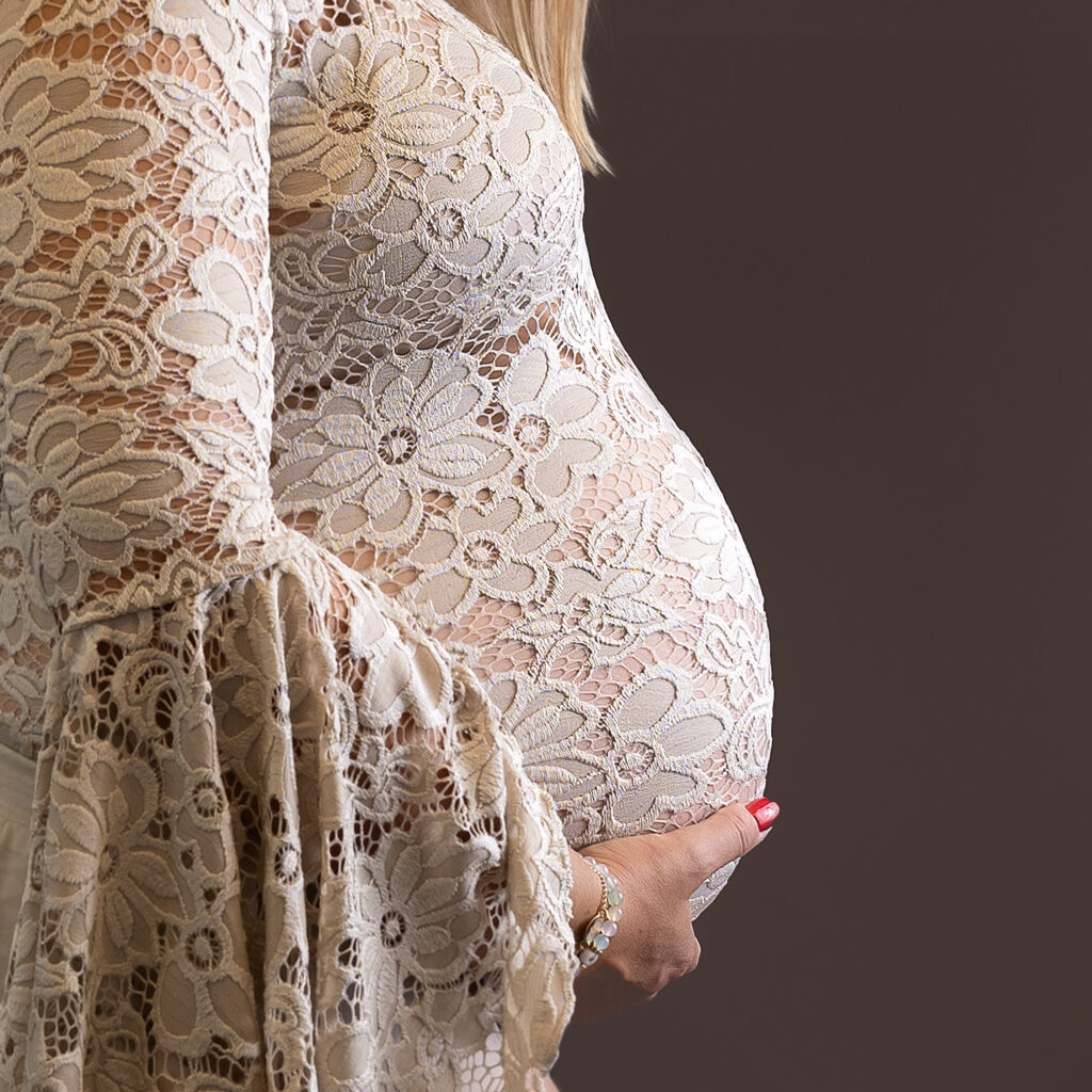 close up foto van de buik van een zwangere vrouw in zand kleurig kanten jurk tijdens een zwangerschap fotoshoot bij Little Miracle memories