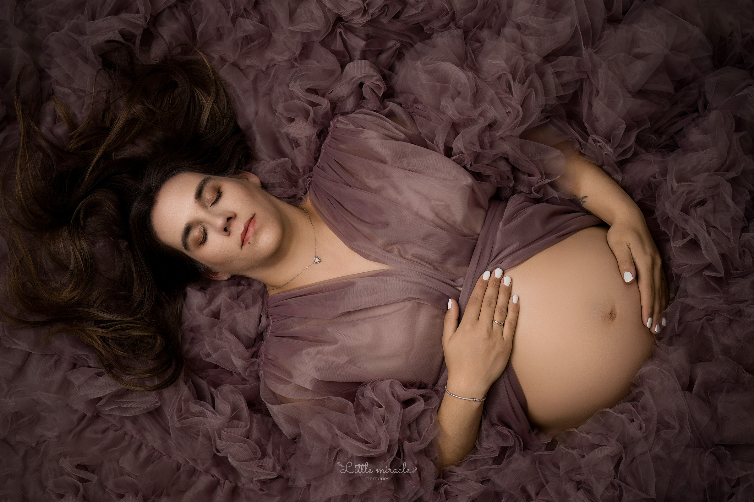 Zwangerschapsportret van een aanstaande mama liggend in zachte tule stoffen, vastgelegd in een luxe fotostudio in Zandhoven